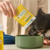Dog eating supplement powder from a yellow packet, with liquid supplement nearby.